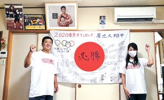 関係者らが寄せ書きした日の丸を飾り、息子を応援した父保さんと母直美さん（左から）＝2日、宜野湾市（提供）