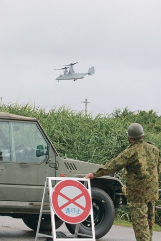 与那国駐屯地グランドから離陸する米軍オスプレイと交通規制に当たる陸自隊員＝23日午前11時50分ごろ、与那国駐屯地体育館前